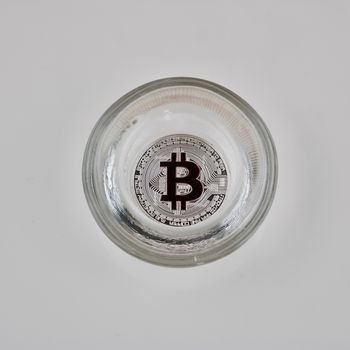 Digital currency physical silver bitcoin coin in glass jar on the white background.