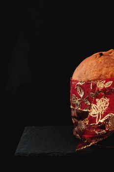 christmas essence, panettone with red ribbon on black background, vertical. Panettone is a typical Christmas cake in Italy