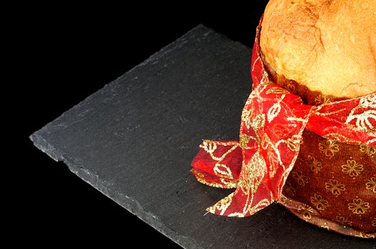 Christmas background, close up on panettone with red ribbon, slate dish on black background. copy space 