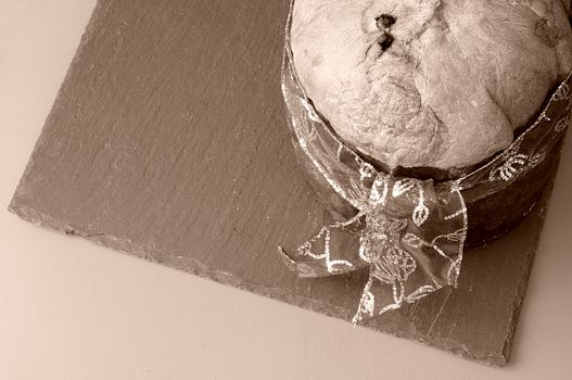 top view of panettone on slate plate, Christmas dessert, typical in italy, made with dough, candied fruit, raisins, with ancient origin in Milan. vintage sepia tone with room for text