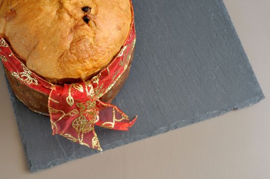 panettone, typical Chirstmas cake, prepared in Italy with long process with simply ingredient, dough, sugar, eggs, candied fruit, raisins. panettone from above with red ribbon on slate dish