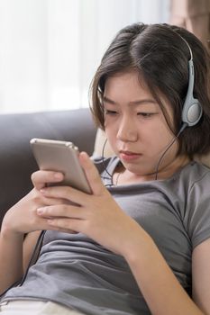 Close up young asian woman short hair listening music from mobile phone on the couch at home