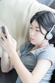 Close up young asian woman short hair listening music from mobile phone on the couch at home