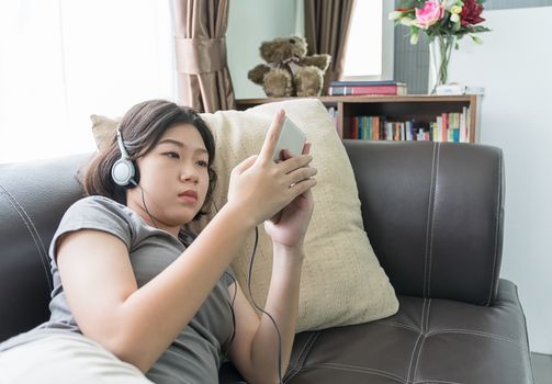 Close up young asian woman short hair listening music from mobile phone on the couch at home