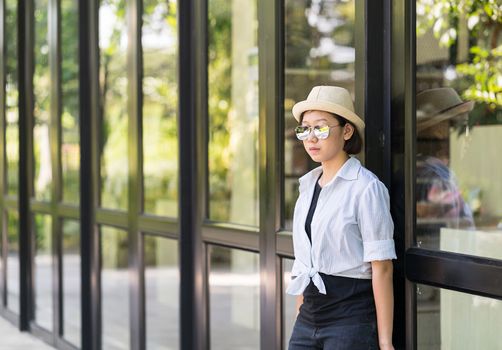 Young women with short hair wearing hat and sunglass standing in front of a glass building