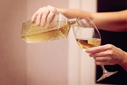 A woman pours a light wine into a wine glass.