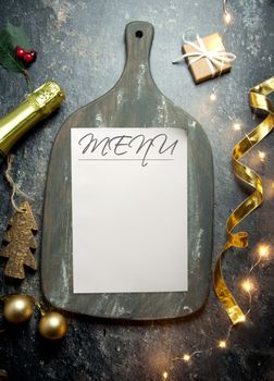 Menu on top of a rustic chopping board with decorations and champagne bottle