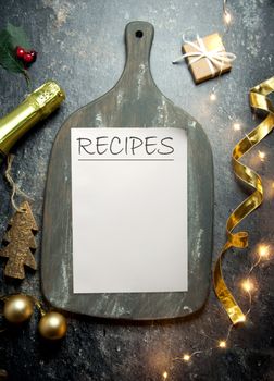 Recipes handwitten on a piece of paper on top of a rustic chopping board with decorations and champagne bottle