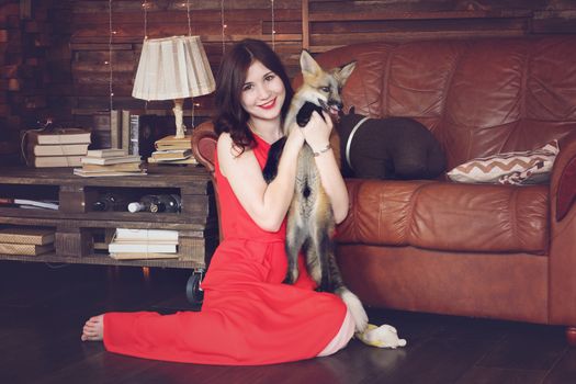 Young beautiful girl in a red dress with a fox in a home setting.