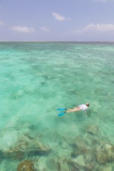 Woman snorkeling in clear shallow sea of tropical lagoon with turquoise blue water and coral reef, near exotic island. Mnemba island, Zanzibar, Tanzania.