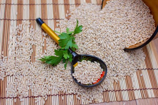 The wooden spoon lies in the scattered pearl barley with a greens branch