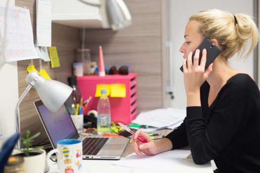 Business and entrepreneurship consept. Beautiful blonde business woman talking on mobile phone in colorful modern creative working environment.