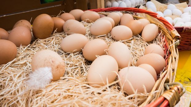 Brown chicken eggs leaning on straw in wooden basket at matket,outdoor.