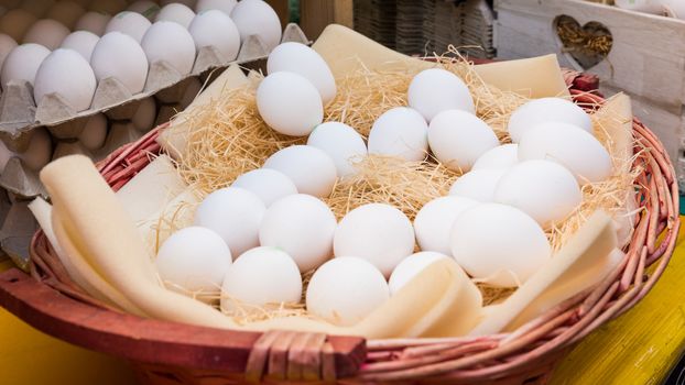 White chicken eggs leaning on straw in wooden basket at market,outdoor.