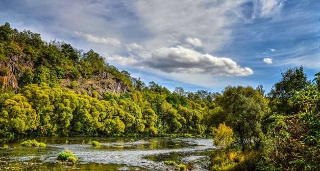A  river flowing peacefully between the trees and the rock.