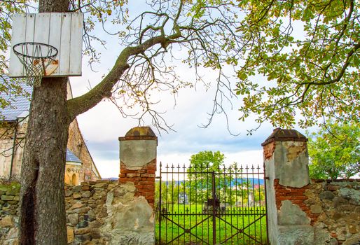 A gates in a cemetery with a basketball basket contrast.