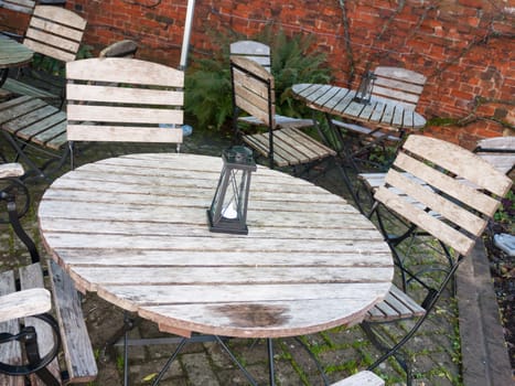 empty wooden public bench table and chairs with black lantern light box and candle ornament; essex; england; uk