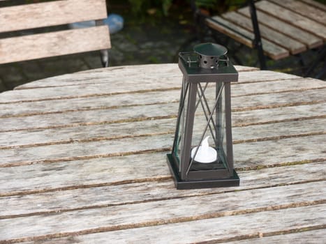 empty wooden public bench table and chairs with black lantern light box and candle ornament; essex; england; uk