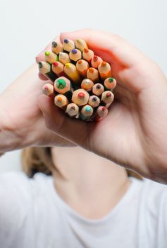 Colored pencils for painting in children's hands on a white background.
