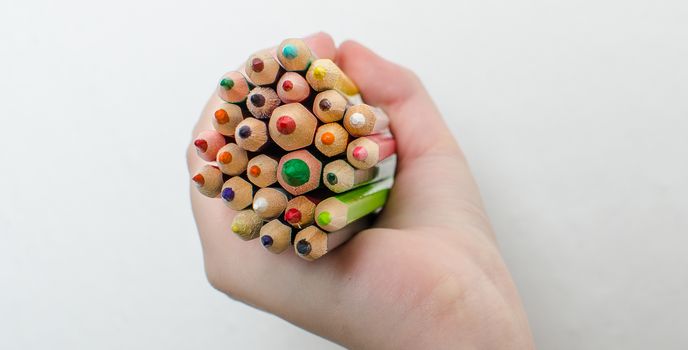 Colored pencils for painting in children's hands on a white background.