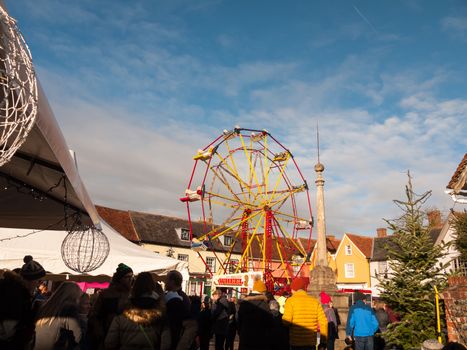 red and yellow carousel wheel outside with people below blue sky christmas fair; essex; england; uk
