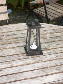 empty wooden public bench table and chairs with black lantern light box and candle ornament; essex; england; uk