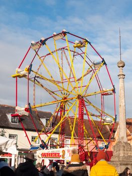 red and yellow carousel wheel outside with people below blue sky christmas fair; essex; england; uk
