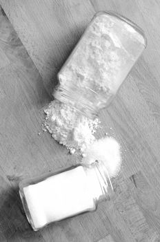 two glass jars overflow sugar and flour on the wooden kitchen table, vertical, Black and white