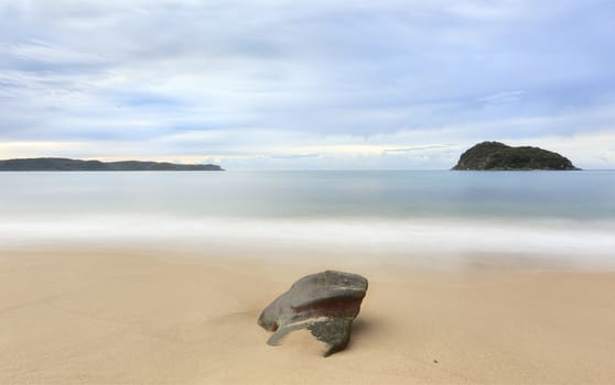 A single rock, a small island and a larger headland feature in a seascape.