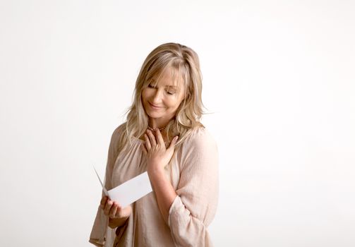 Woman reading a heartfelt message, note, book or card.   She is smiling and has her hand to heart. White background