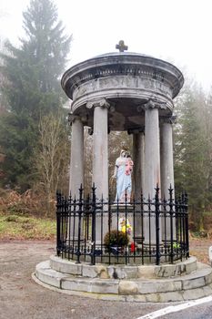Statue of the virgin and baby Jesus under a monument in the forest at a misty temp in province of Luxembourg in Belgium