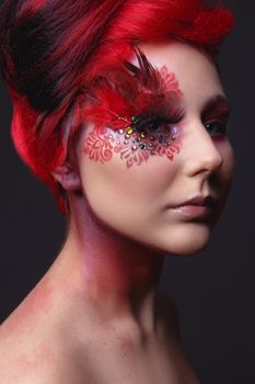 Portrait of a beauty young  girl with red hair.  Creative ingenious makeup with feathers, rhinestones and large eyelashes