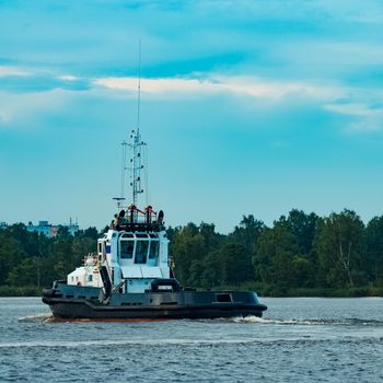 Black tug ship moving to the cargo terminal. Industrial service