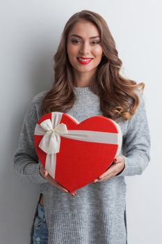 Young girl with red heart-shaped gift box on white background