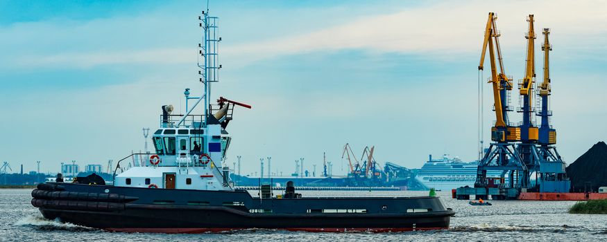 Black tug ship moving to the cargo terminal. Industrial service