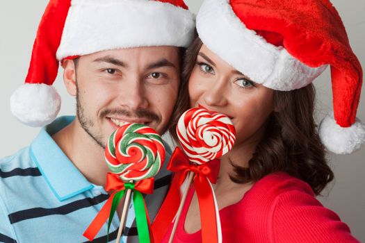 Young happy funny couple in christmas santa hats with lollipops