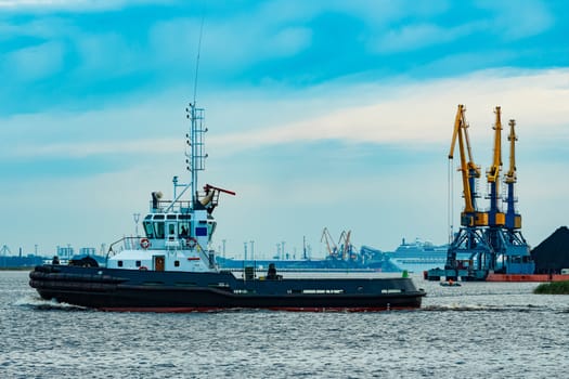 Black tug ship moving to the cargo terminal. Industrial service