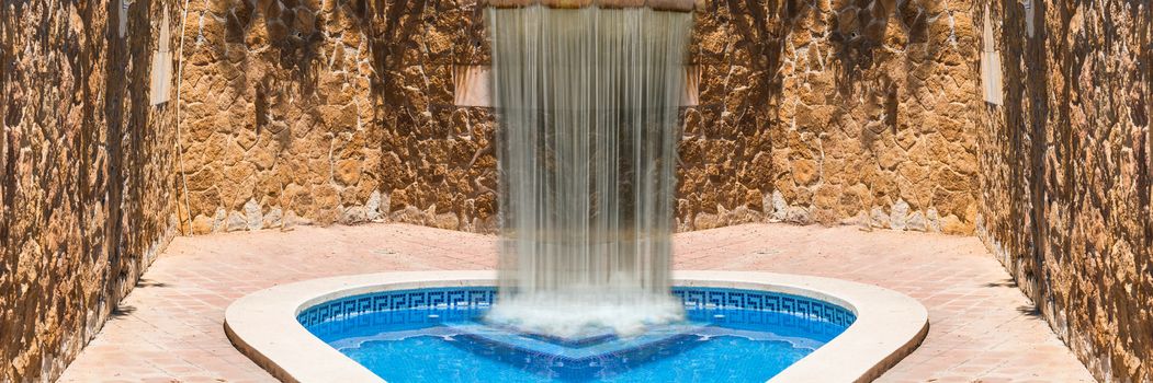 Luxury swimming pool with waterfall. In the background a mediterranean wall decorated with sandstones.