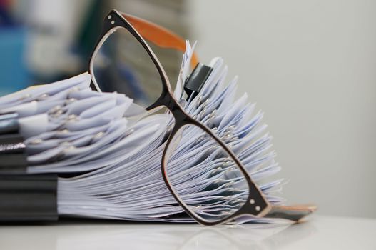 Unfinished document, stacks of paper files with clips on desk for report and glasses in the office at morning, Business offices concept on workplace background.