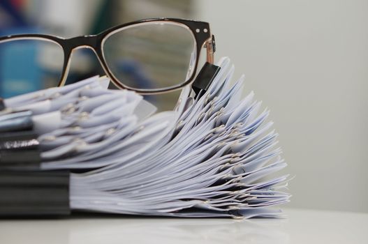 Unfinished document, stacks of paper files with clips on desk for report and glasses in the office at morning, Business offices concept on workplace background. 