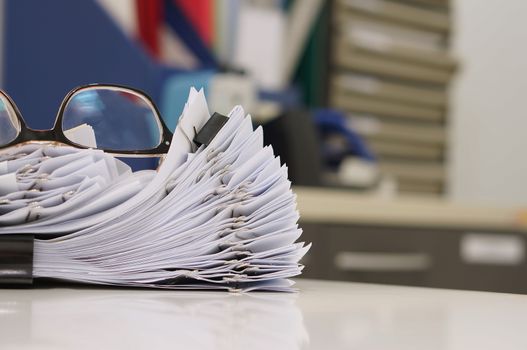 Glasses placed on finished document, stacks of paper files with clips on desk for report in the office at morning, Business offices concept.                               