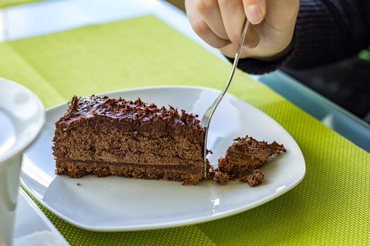 A girl's hand breaks a piece of chocolate cake on a plate. Close Up