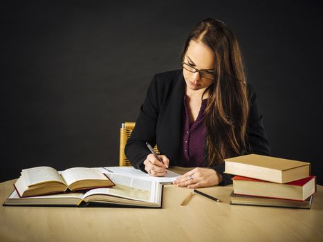 Photo of a teacher or business woman in her 30's sitting at a desk in front of a large blackboard writing.