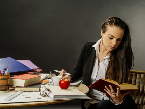 Photo of a teacher or business woman in her 30's sitting at a desk in front of a large blackboard reading.