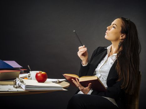 Photo of a teacher or business woman in her 30's sitting at a desk in front of a large blackboard thinking.