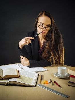 Photo of a teacher or business woman in her 30's sitting at a desk in front of a large blackboard thinking.