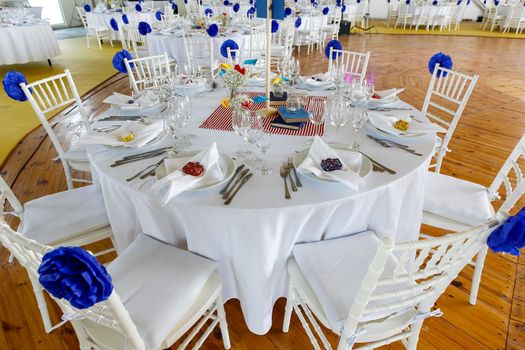 Circle dinner table served with white crockery and decorated with colorful objects.