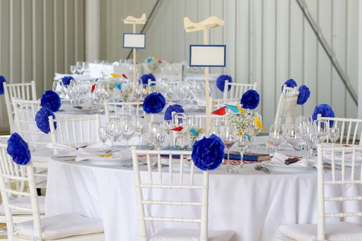 Circle dinner table served with white crockery and decorated with colorful objects.