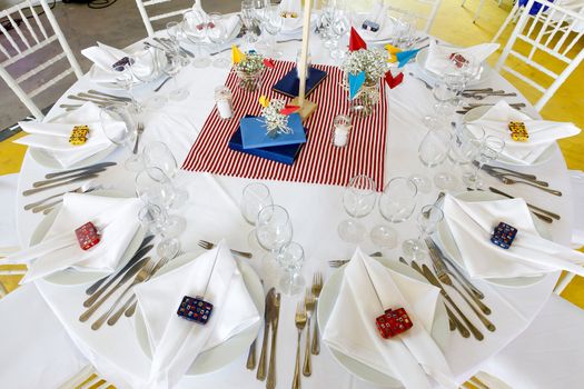 Circle dinner table served with white crockery and decorated with colorful objects.