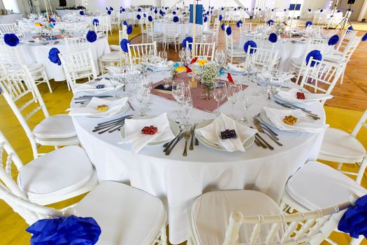 Circle dinner table served with white crockery and decorated with colorful objects.